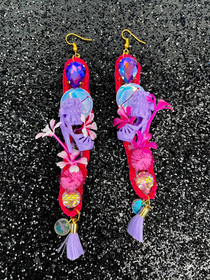 Pink long thin crochet shape, dangle earrings. With purple twinkly stones, iridescent sequins, miniature dolls shoes, flowers, pom poms and lilac tassels