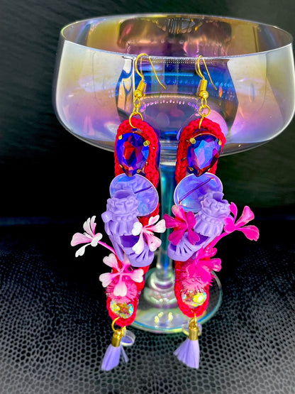 Pink long thin crochet shape, dangle earrings. With purple twinkly stones, iridescent sequins, miniature dolls shoes, flowers, pom poms and lilac tassels. Pink and purple shoe lovers heaven.