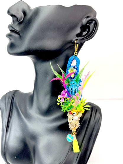 Long blue crochet earring with an aquarium theme, including aquarium plants with glitter. Small blue glass octopus, tiny yellow glass fish, with tiny gravel at the bottom small seashells and a large real pearl. It looks like an authentic scene of an aquarium for your ears