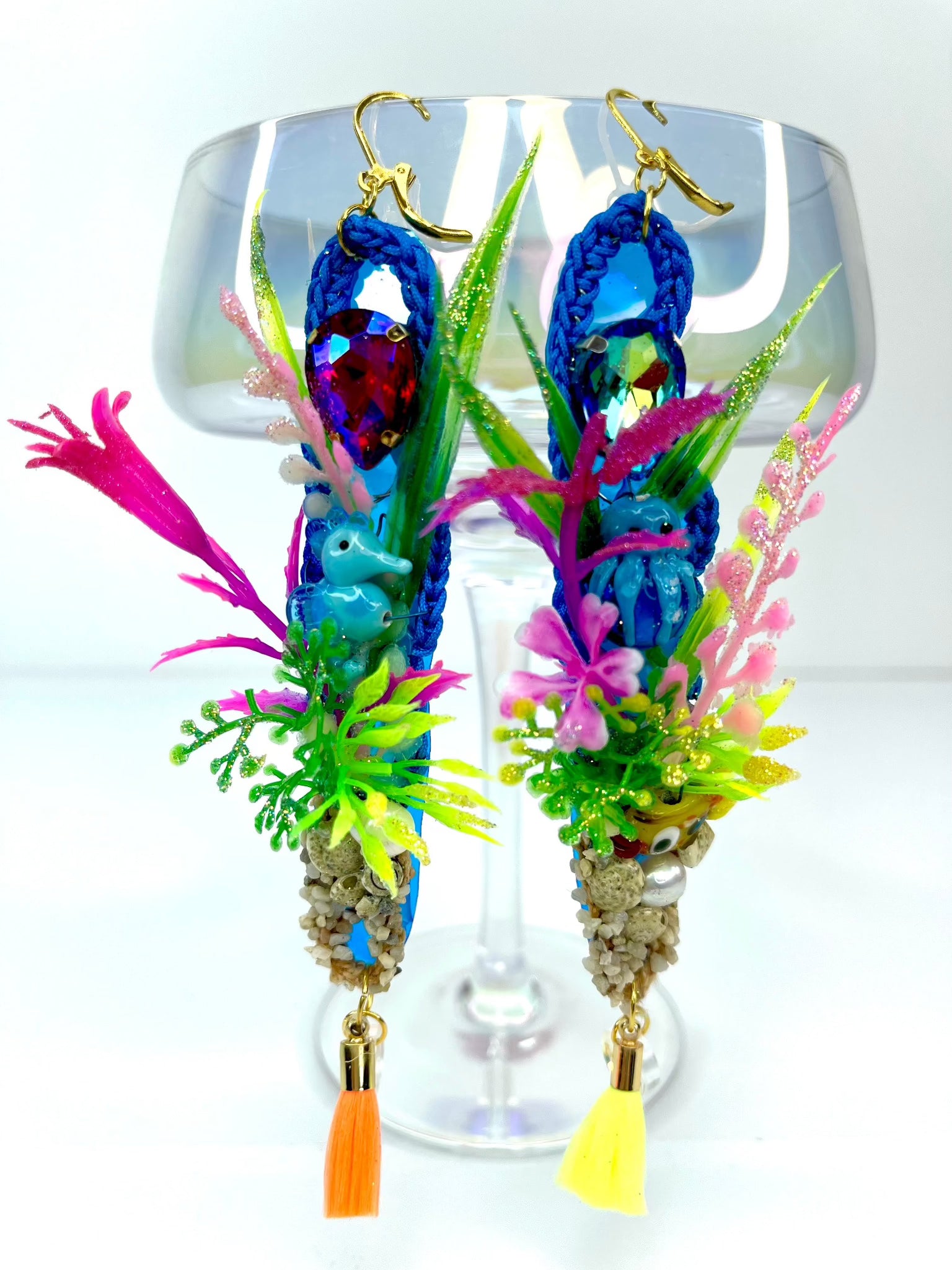 Blue crochet earrings in a long oval shape of 12cm, with a colourful under the sea theme including aquarium plants, glass seahorse, small gravel with seashells real pearl and small tassel. 2nd earring is similarly themed with aquarium plants, blue glass octopus and tiny yellow glass fish, with gravel pearl and mismatching yellow and orange tassels